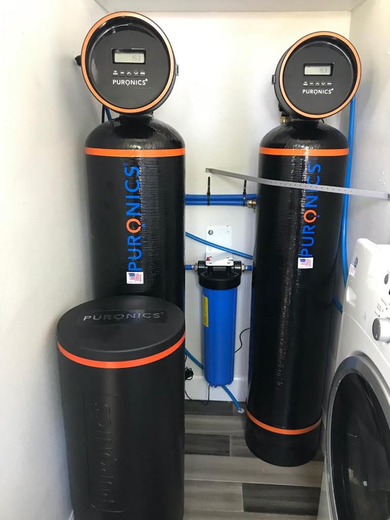 Installed whole-home water filtration tanks and control valves in a residential utility area.